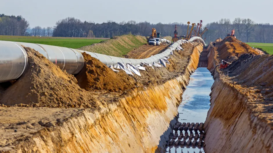 Man sieht auf eine Baustelle mit viel aufgerissener Erde, einer großen Vertiefung für bereitliegende Rohre und Baufahrzeuge